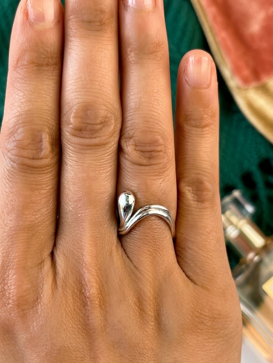 A close-up of a hand wearing a polished silver ring with a unique, intertwined loop design on the ring finger.