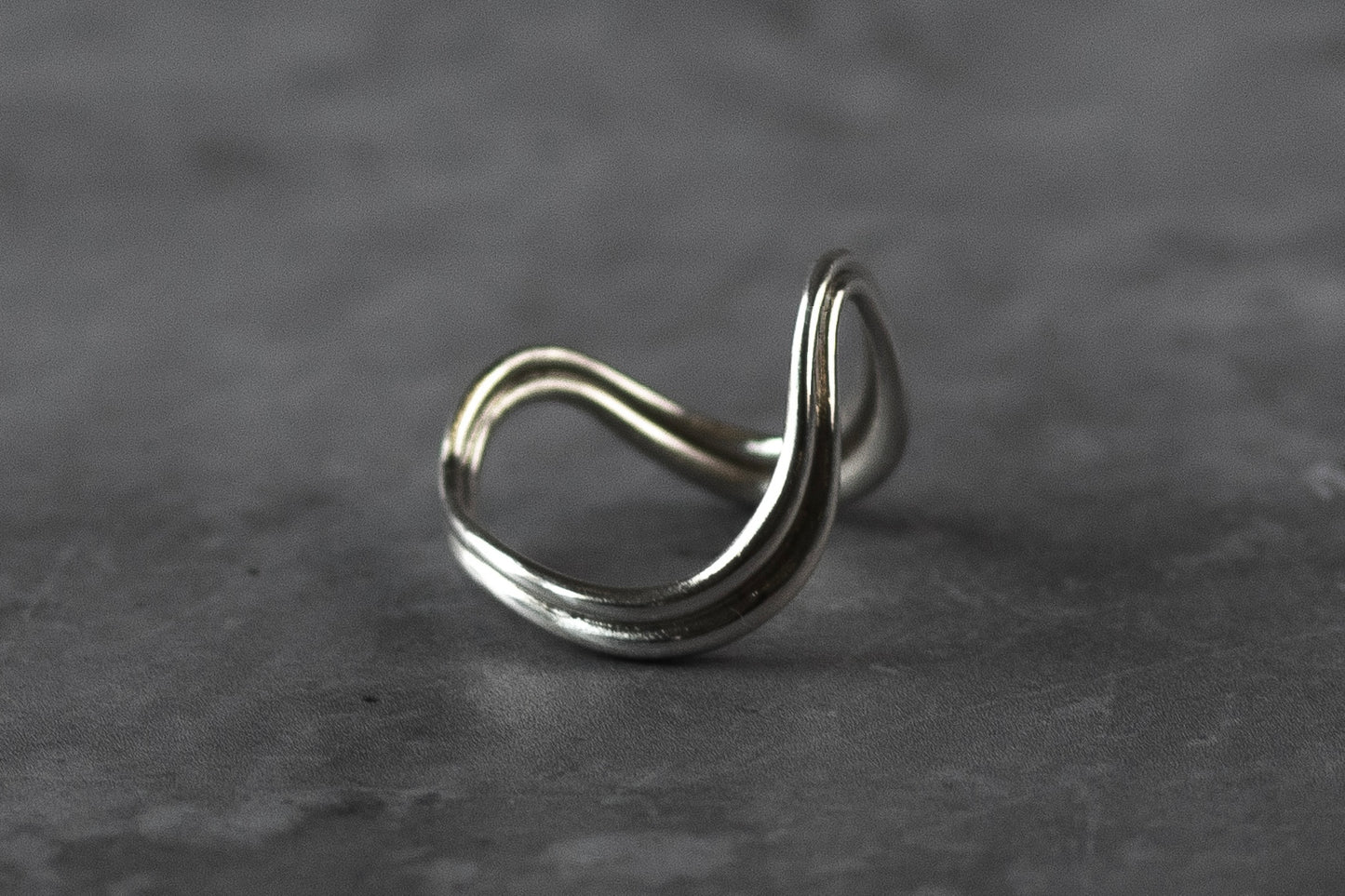 Certified London Hallmarked .925 Sterling Silver wave ring with a unique looped design, resting on a textured dark grey surface.